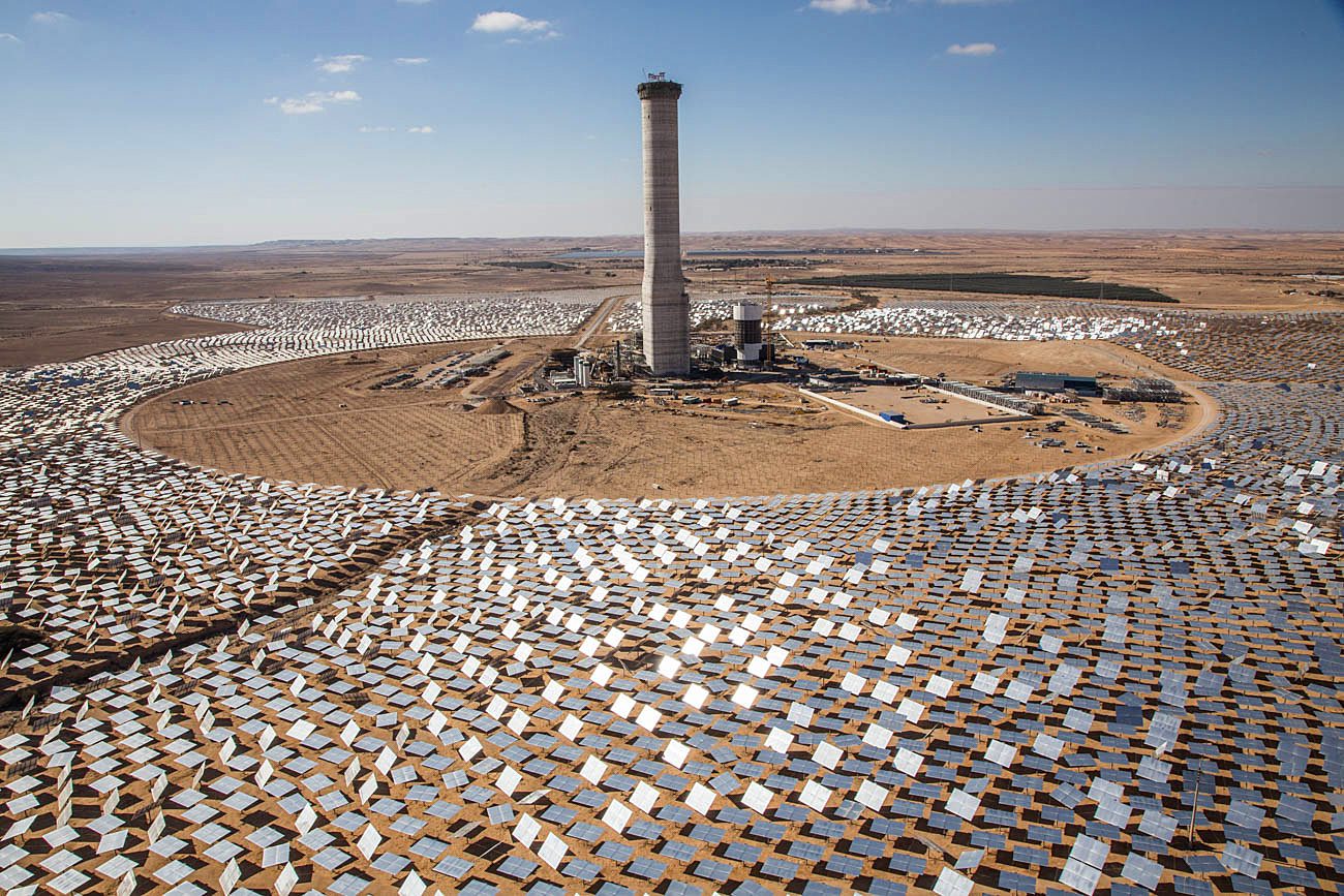 A solar power tower stands in the desert surrounded by a sea of mirrors in a cricle around it all facing it to reflect the sun