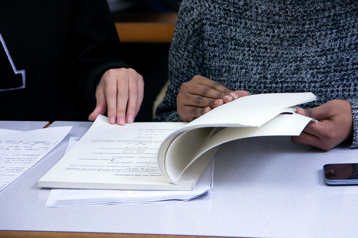 Close up of two people flicking through a workbook together.