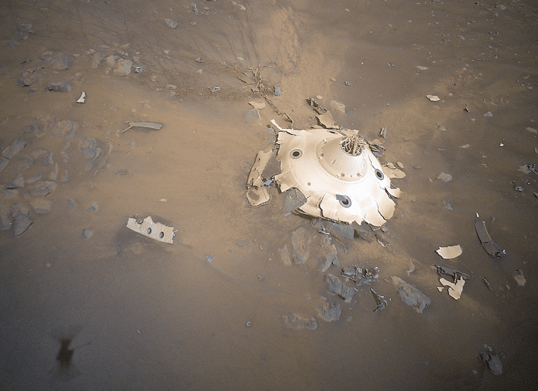 A smashed, round, white metal object on the surface of Mars.