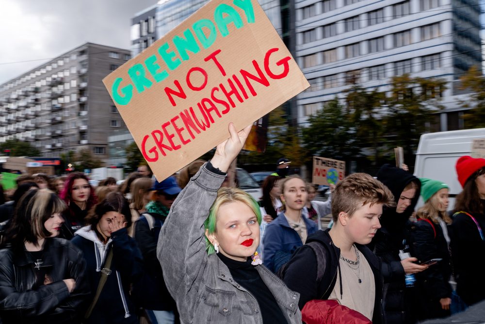 Young woman holding a sign at a climate protest against greenwashing