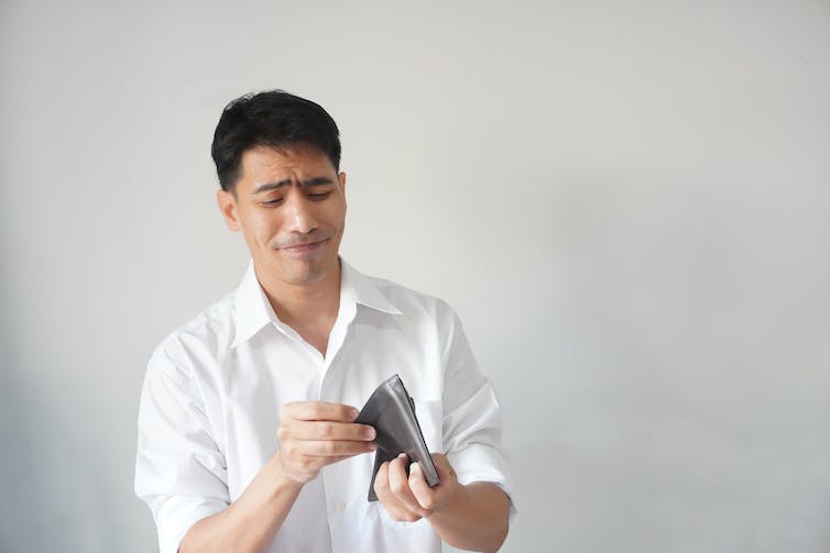 Image of a man looking at his empty wallet, unhappy.