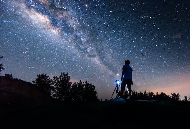 Silhouette of person looking up at a night sky next to camera.