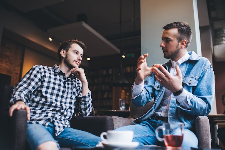 From below young men in casual outfits sitting on chairs at table with tea and coffee discussing together