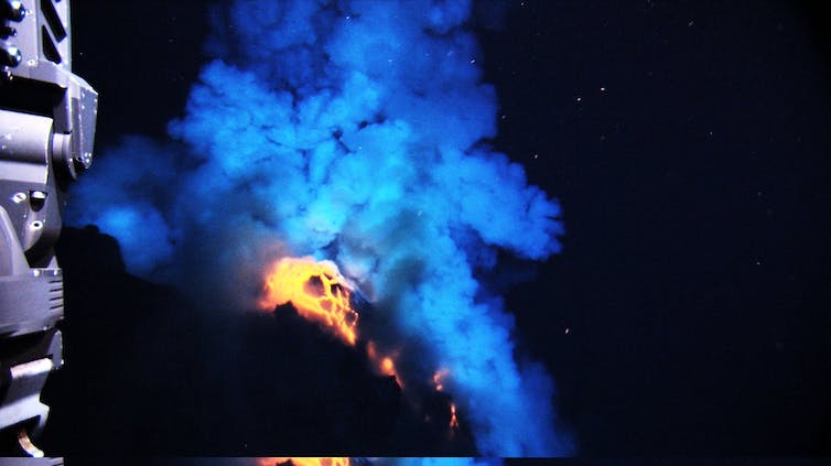 An underwater photo showing smoke above glowing lava on the seafloor.