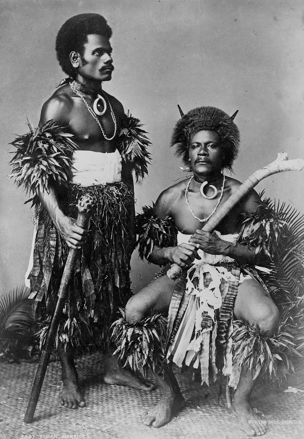 Two Fijian individuals pose with their clubs for an 1884 portrait.