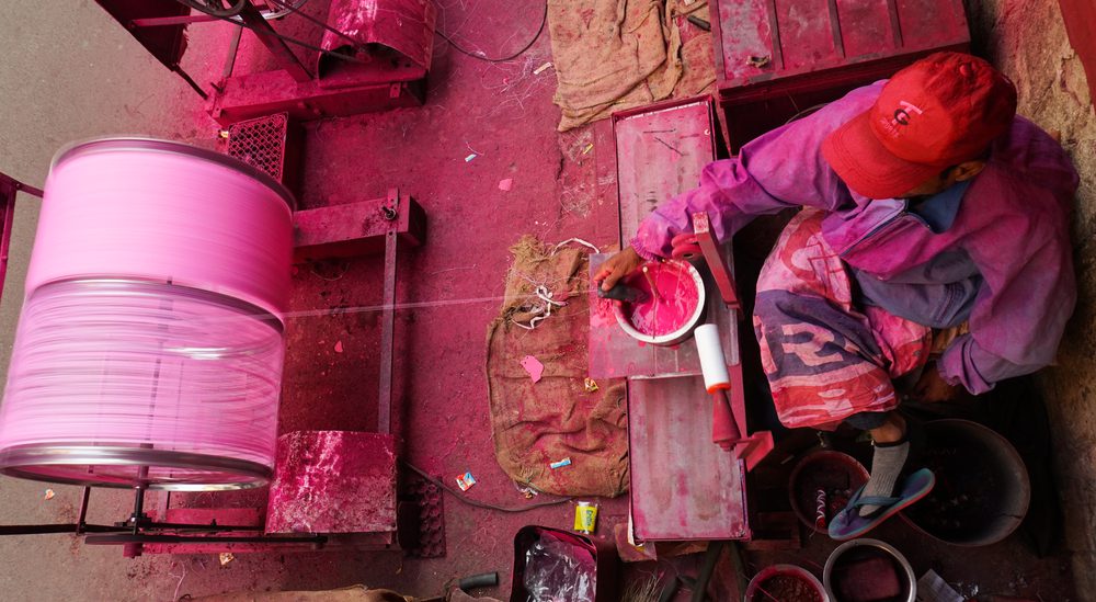 worker applying pink powdered glass mixture to kite string