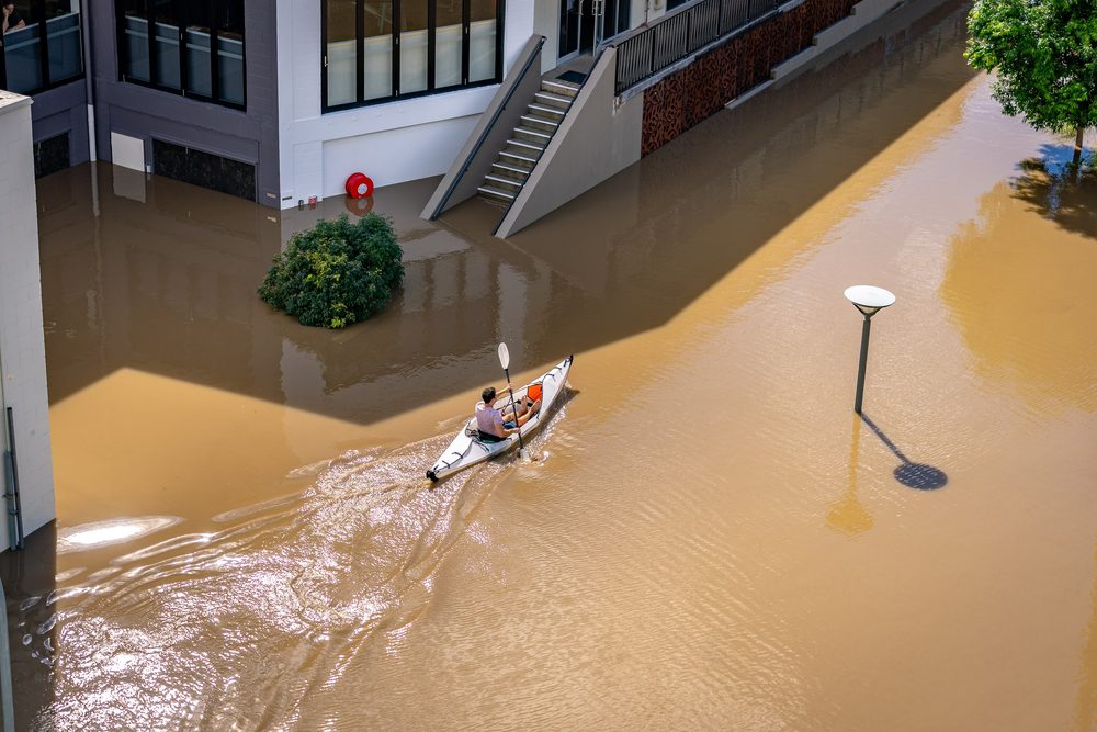 Man kayaking in the water flooded streets of Brisbane, Australia during 2022 wet season.