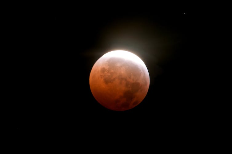 A moon shaded orange with a brighter white edge on top on a black background