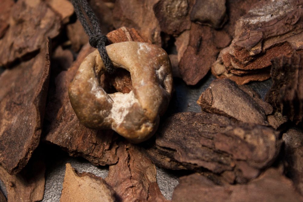 hag stone tied to a cord on a background of wood chips