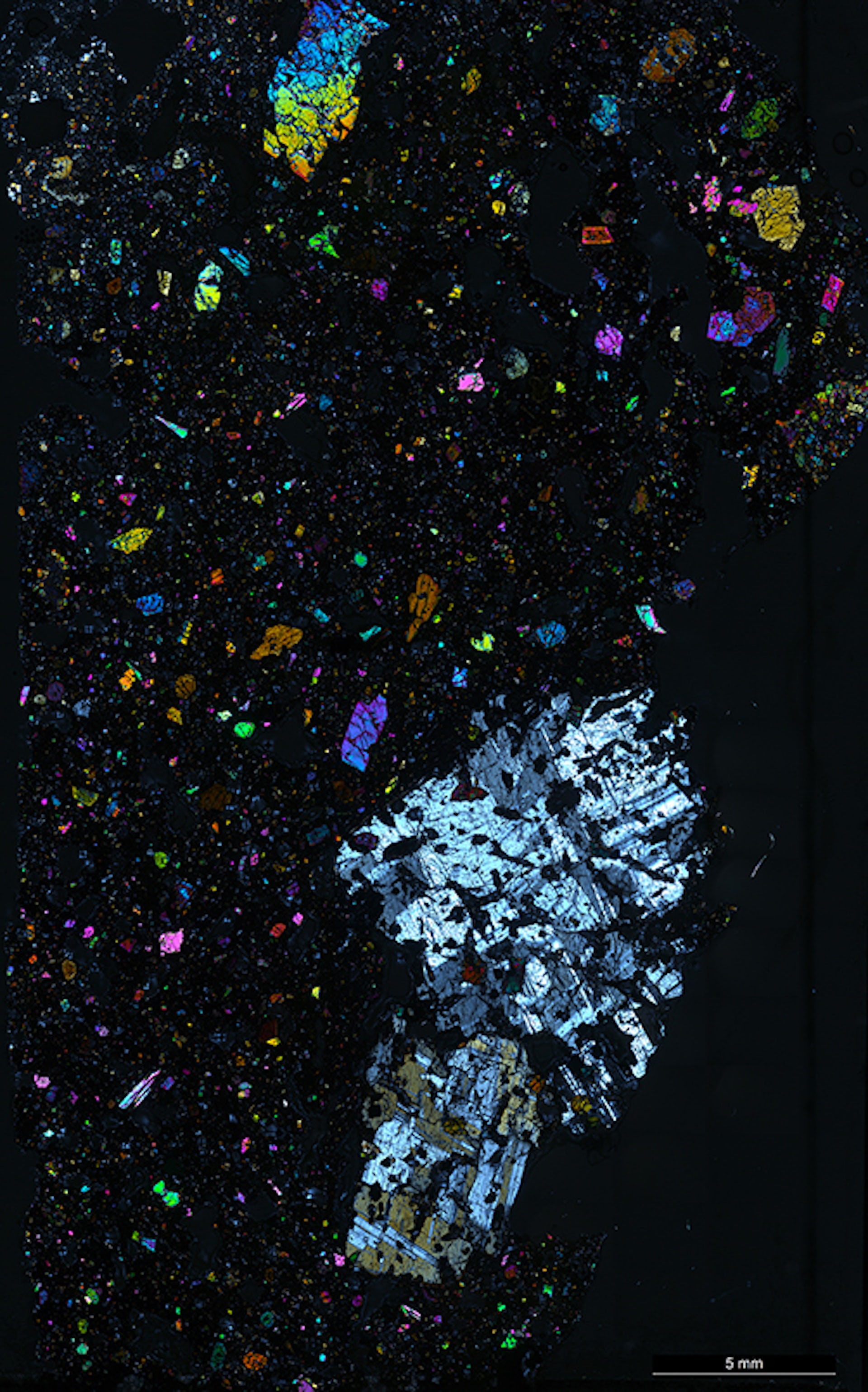 Microscope view of lava, with large colourful crystals in a fine-grained black rock matrix