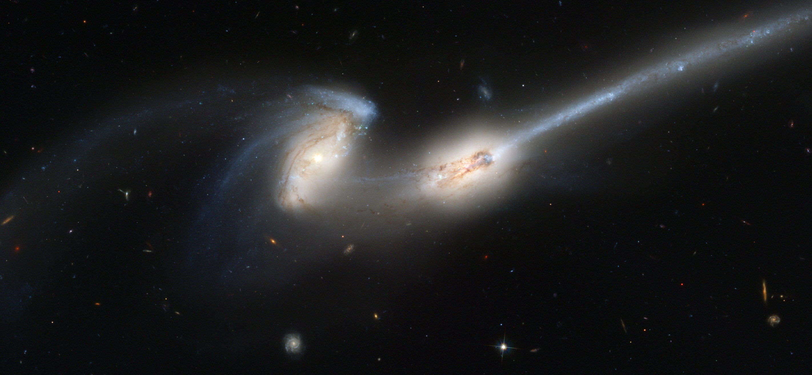 two colliding galaxies with long tails of material stretching in a thin line behind them like a mouse tail