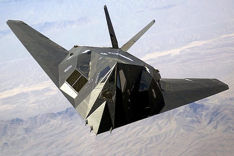 a single-seat odd-shaped jet aircraft flies high above the desert