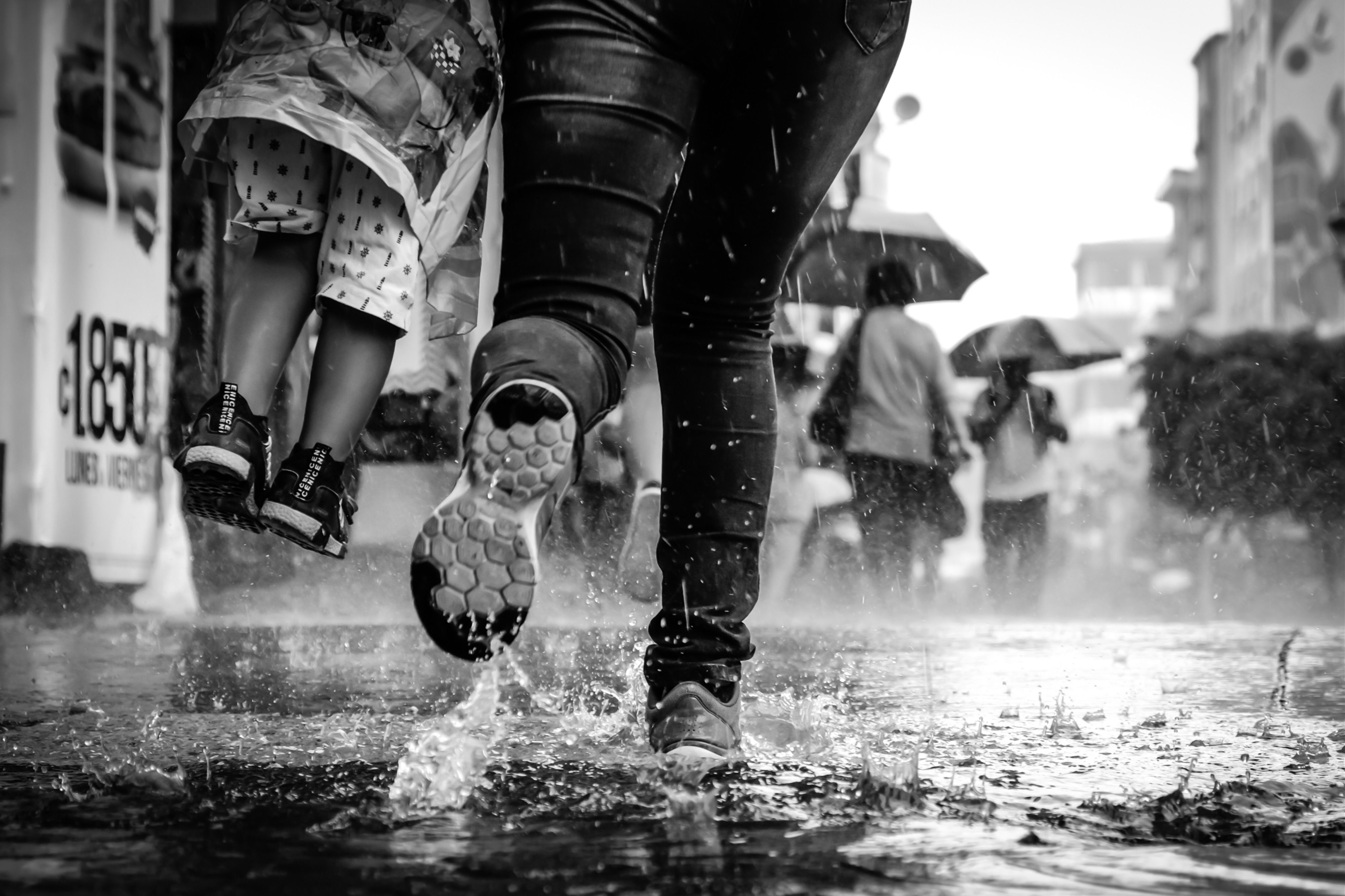 black and white photo of child's legs being carried as adult runs along rainy street