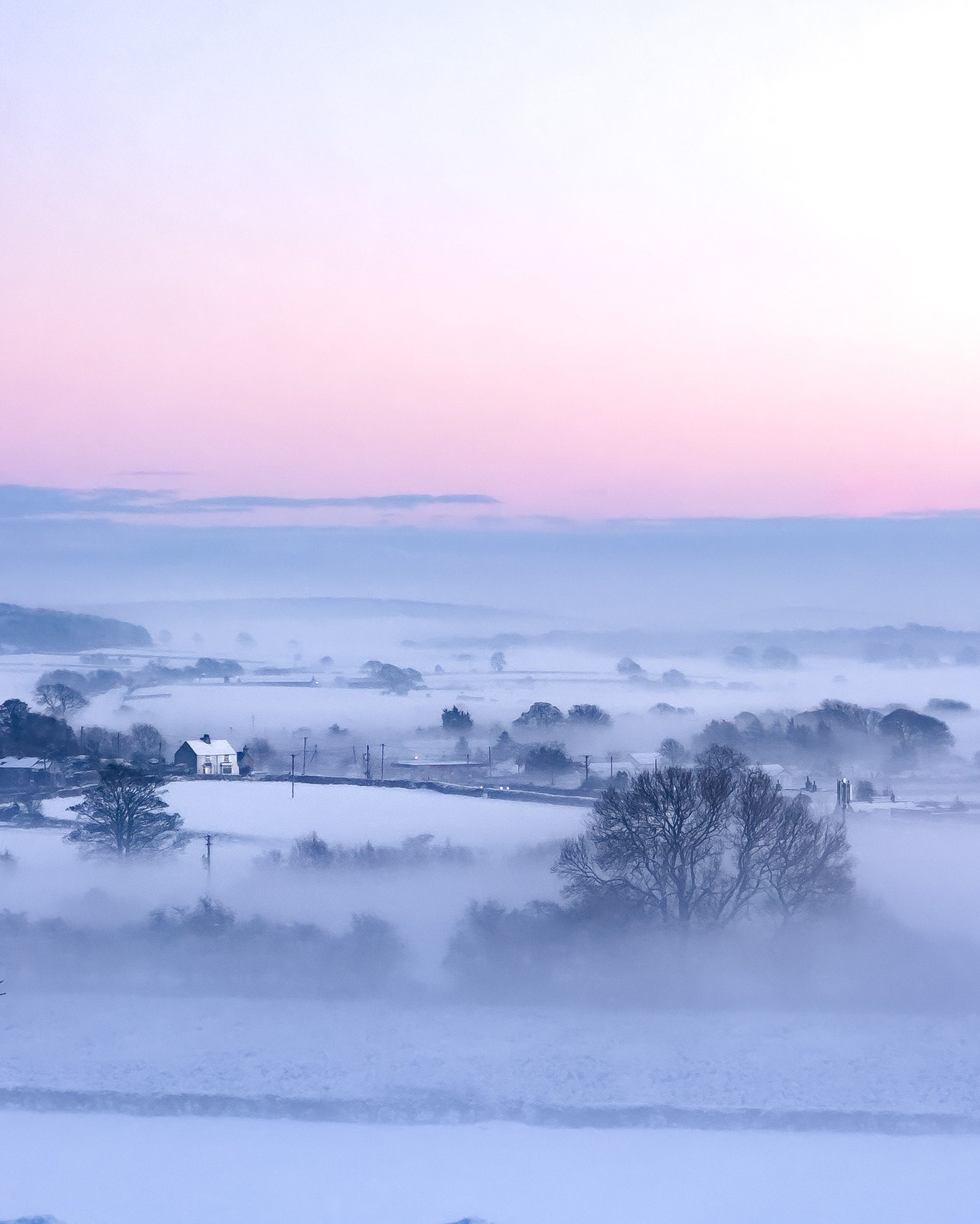 View over snowy Welsh village with mist and pink sky