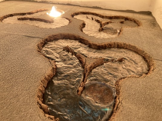 three waving triangles are seen melted among the sandy material. One of them is still shining as the laser is still on it.