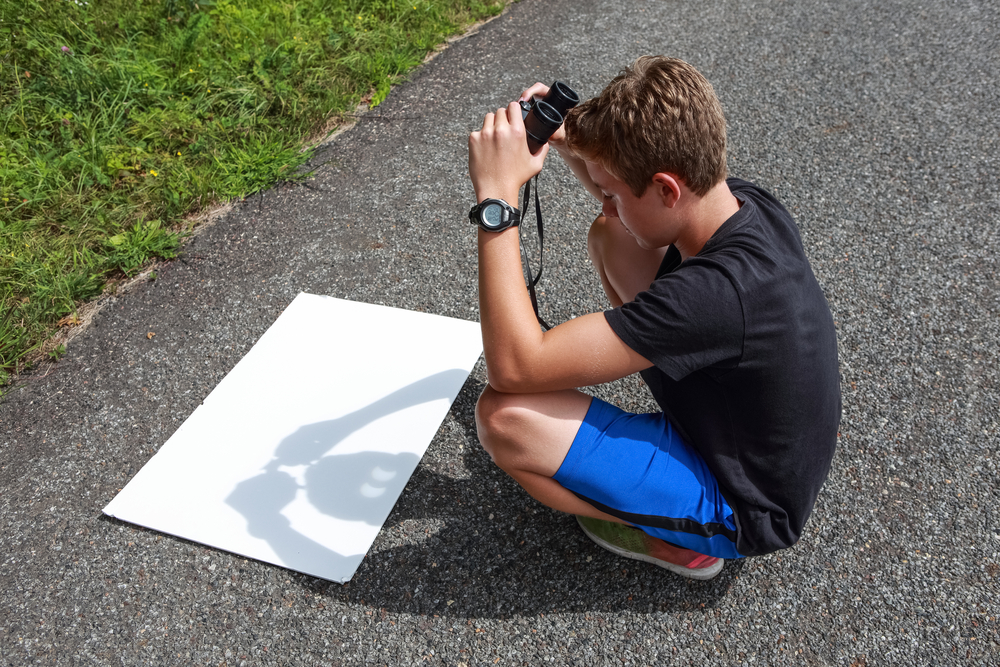 Boy holding binoculars to make a reflection of the sun during a solar eclipse