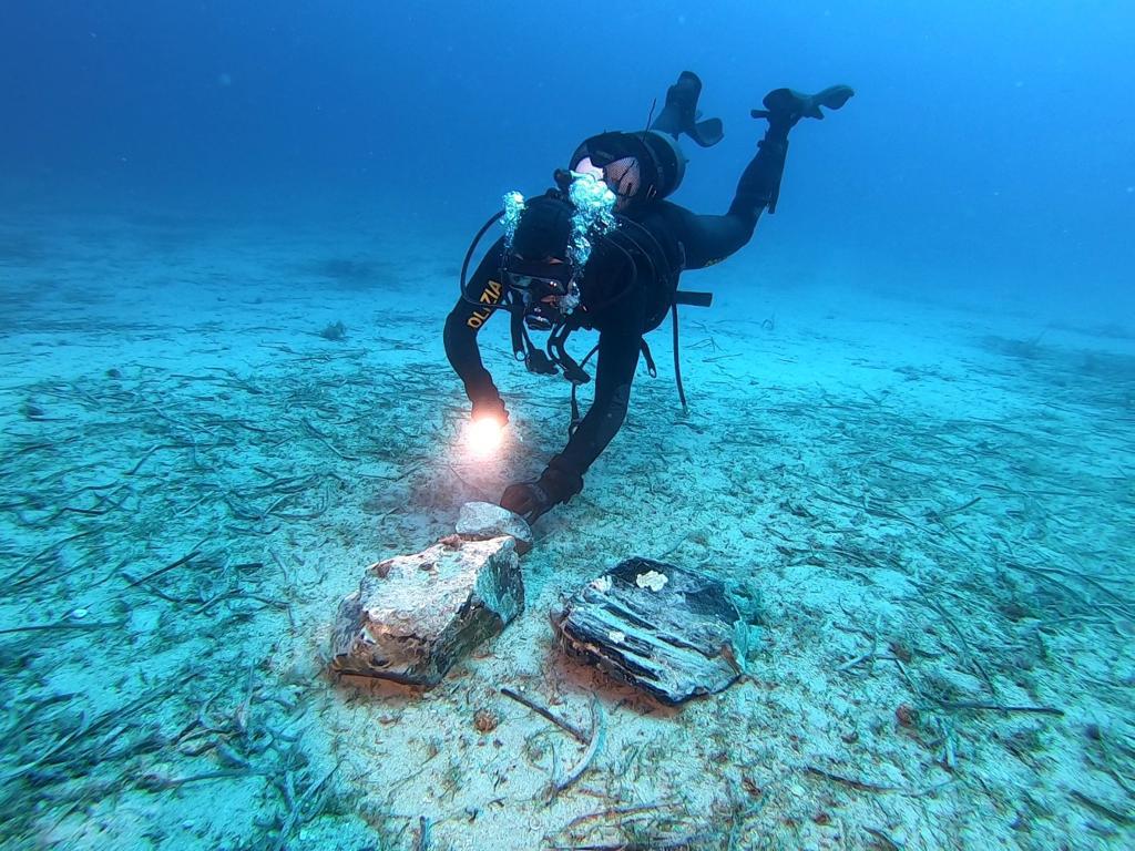 A diver above the seabed looking down at two large chunks of obsidian - black shiny volcanic glass