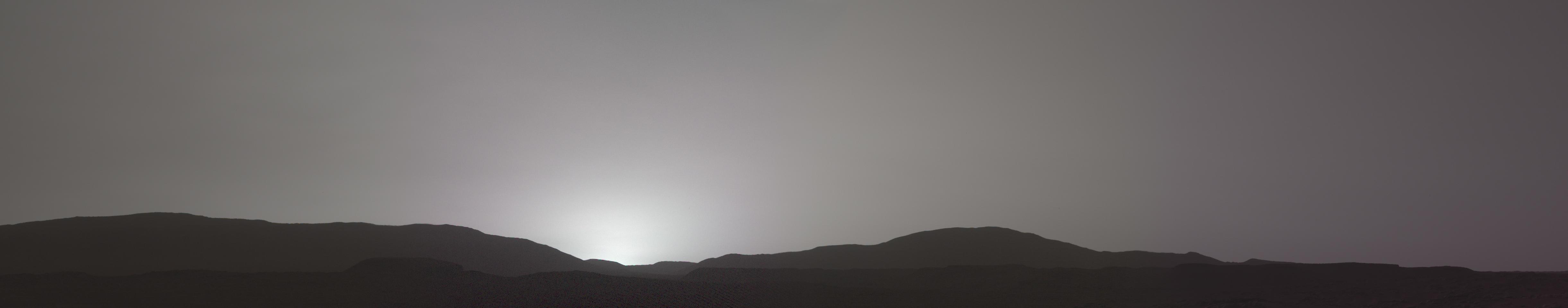 The profile of hills in jezero crater hide the Sun bright beyond the horizon. The sky is a greyish color The profile of hills in jezero crater hide the Sun bright beyond the horizon. The sky is a greyish color