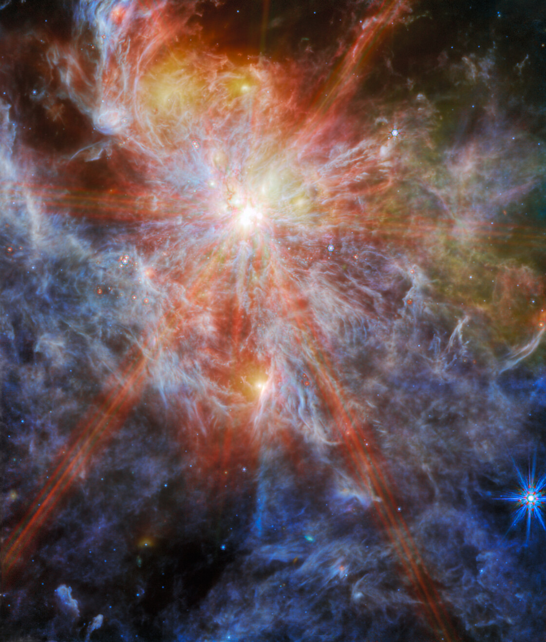 A bright young star within a colourful nebula. The star is identifiable as the brightest spot in the image, surrounded by six large spokes of light that cross the image. A number of other bright spots can also be seen in the clouds, which are shown in great detail as layers of colourful wisps