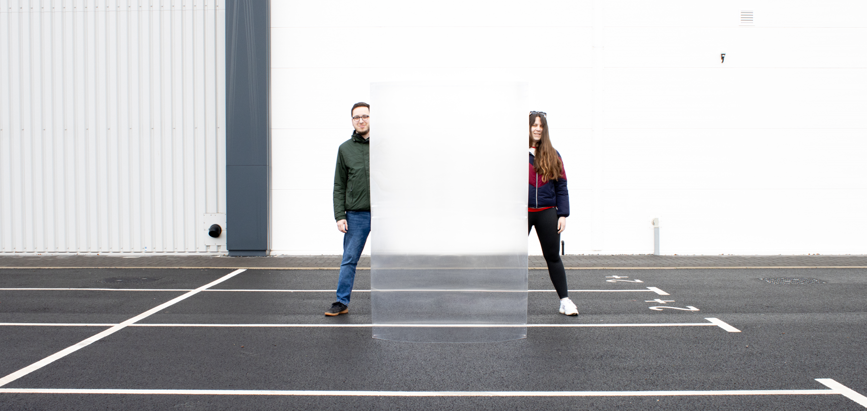 A man and woman standing behind an invisibility shield in a carpark.