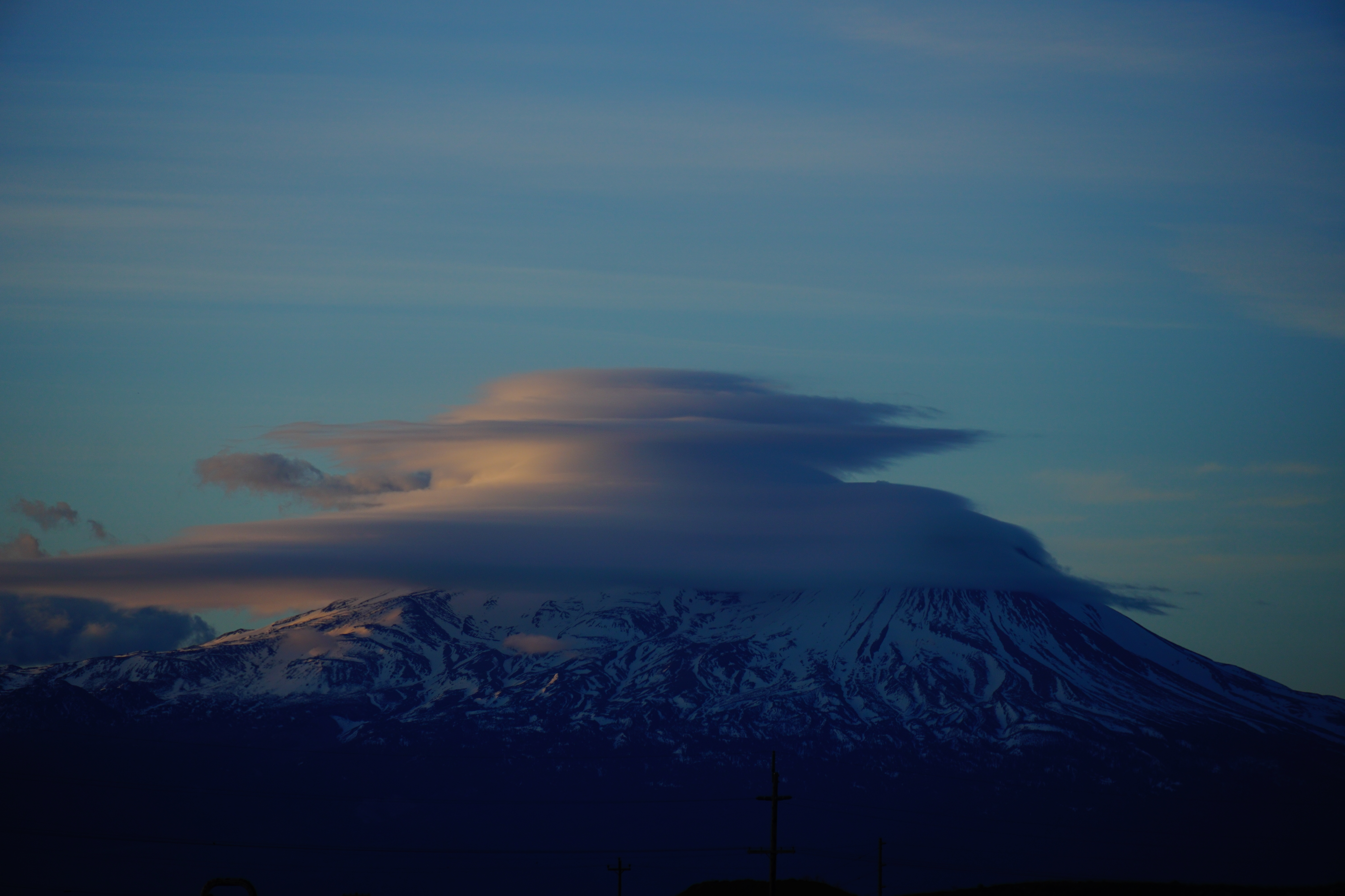 snow-capped mountain with the top partly obscured by a round cloud formation at sunset