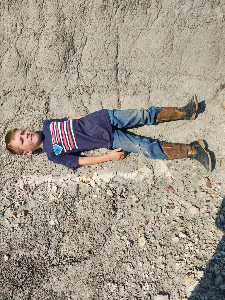 Liam Fisher lying next to his discovery - the leg bones of a T.rex