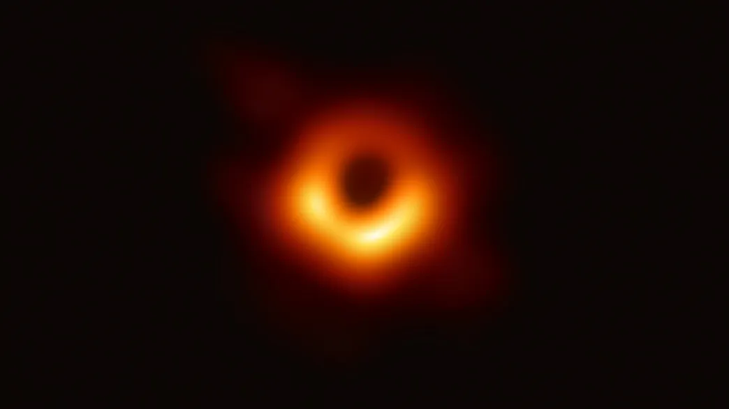 a fuzzy orange irregular donut is a the center of the screen, the shadow of the black hole