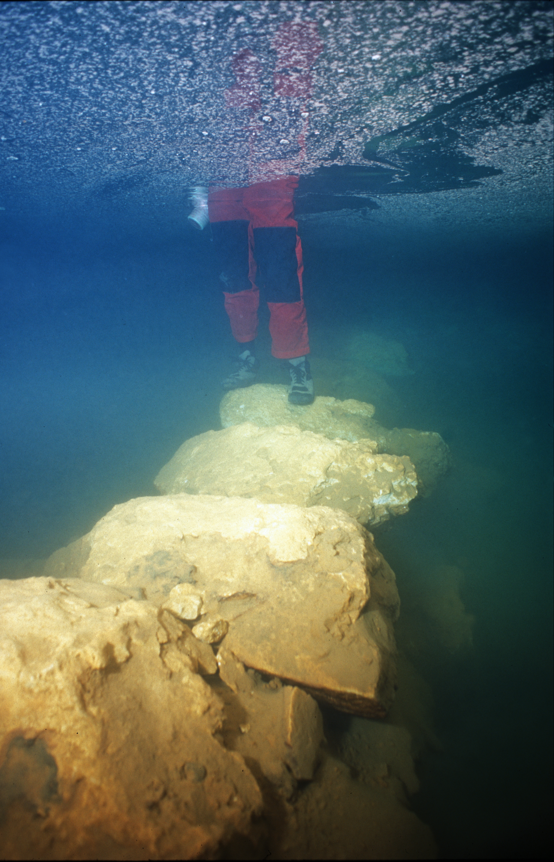 close up of someone's legs and feet standing on a submerged stone bridge