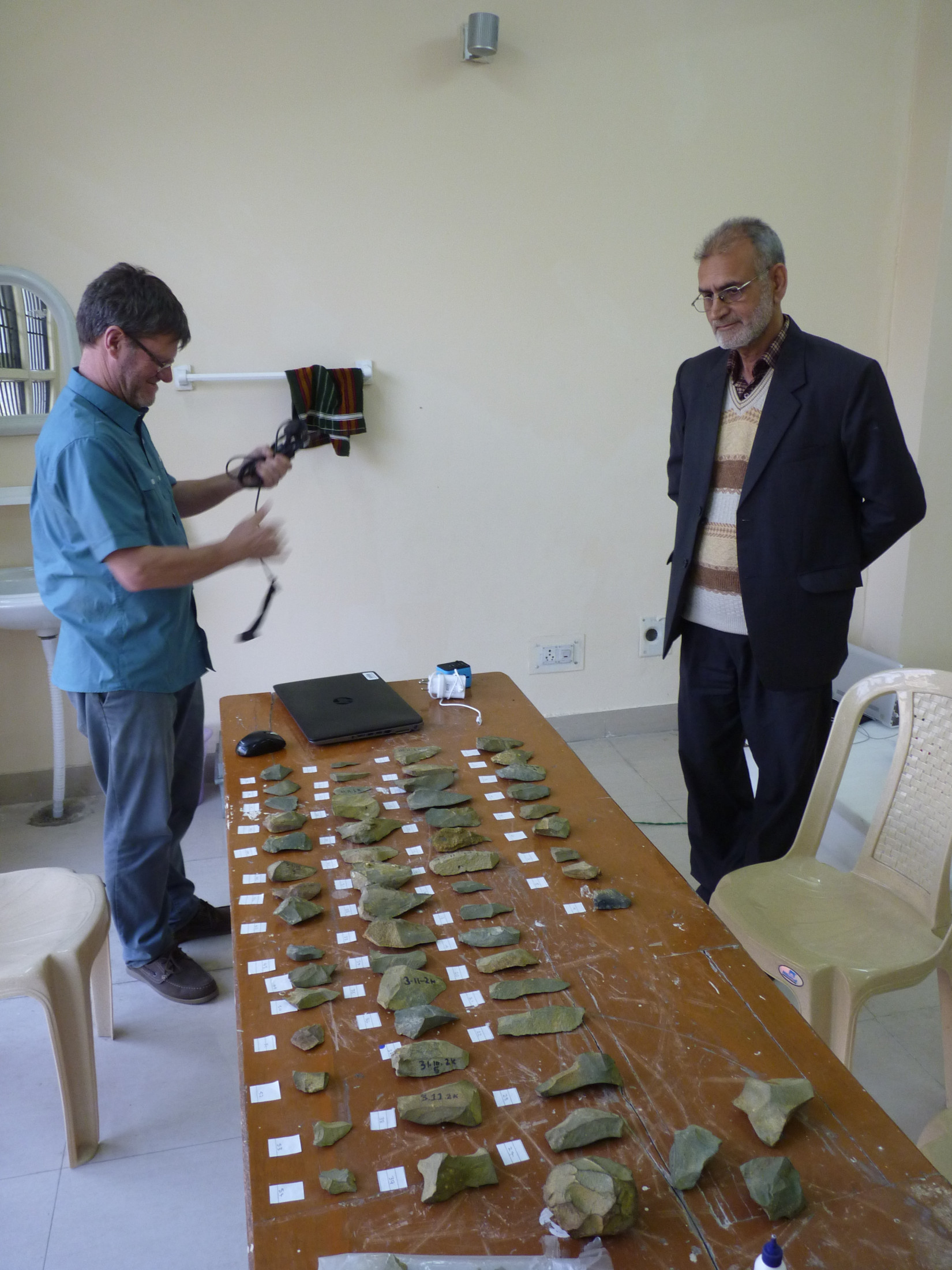 Two researchers stand on either sides of a table full with labelled stone tools from the site.