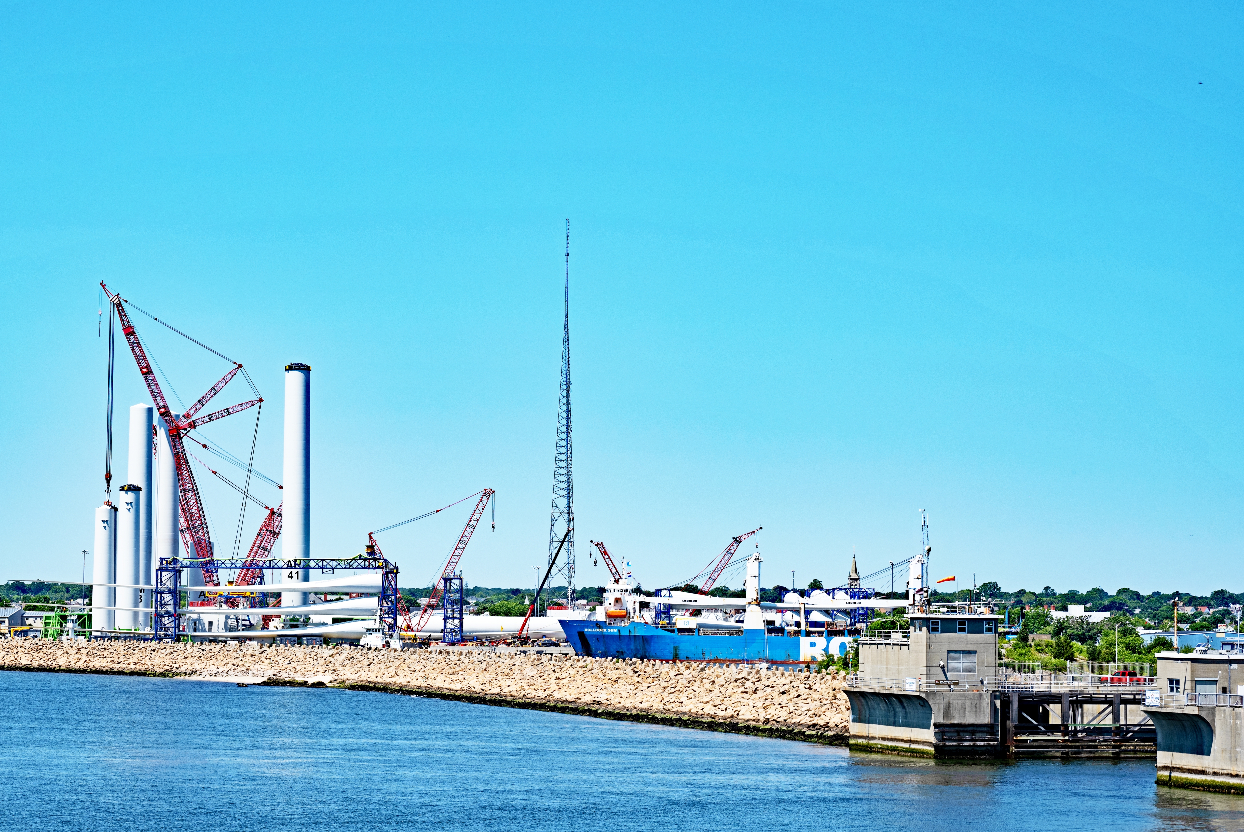 New Bedford, Massachusetts - July 2 2024: the hurricane barrier at the entrance to the port of New Bedford with the assembly facility for the wind turbines for Vineyard Wind 1 in the background.