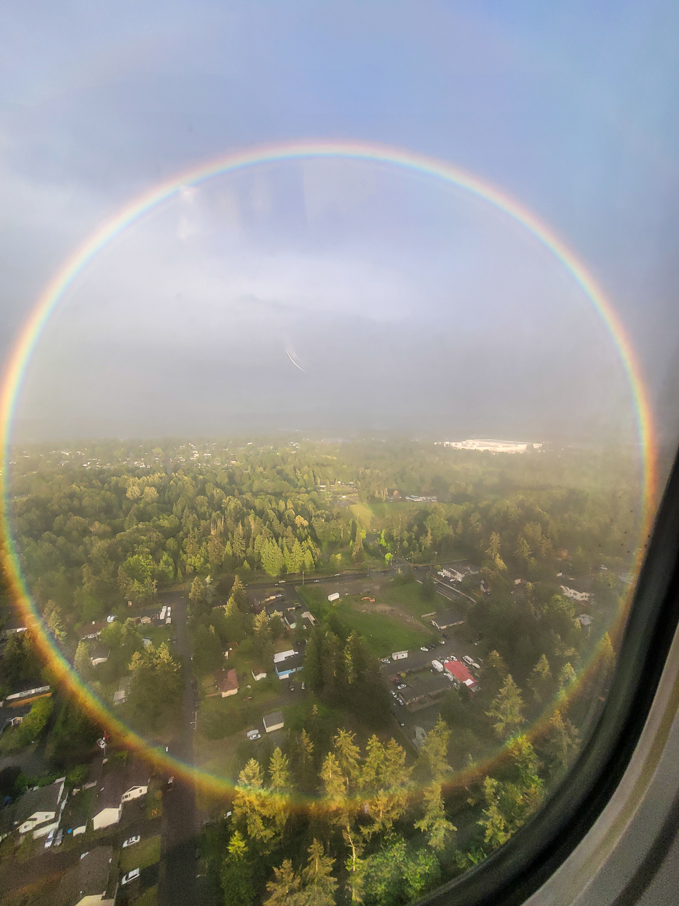 A Circular Rainbow appears in the rain across a green landscape.