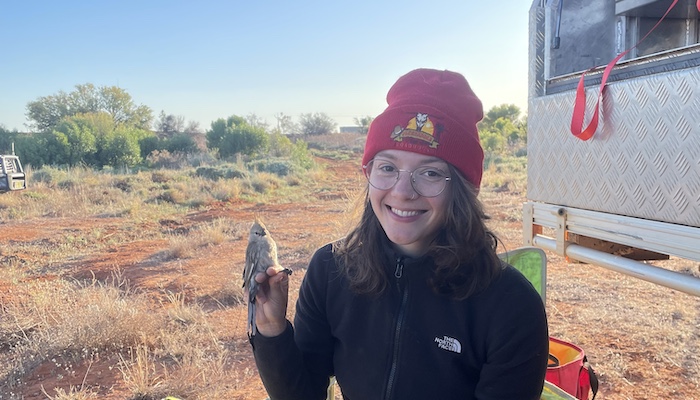 Smiling person in red beanie hat holding a small bird