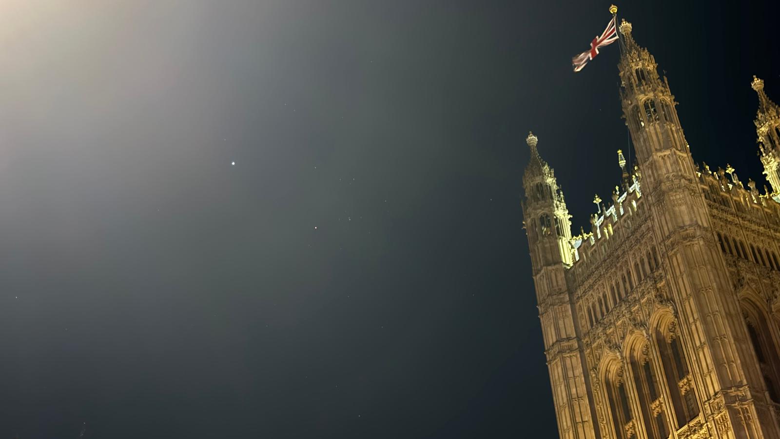 The Victoria tower is visible flying the Union flag. In the sky, two bright dots of light.