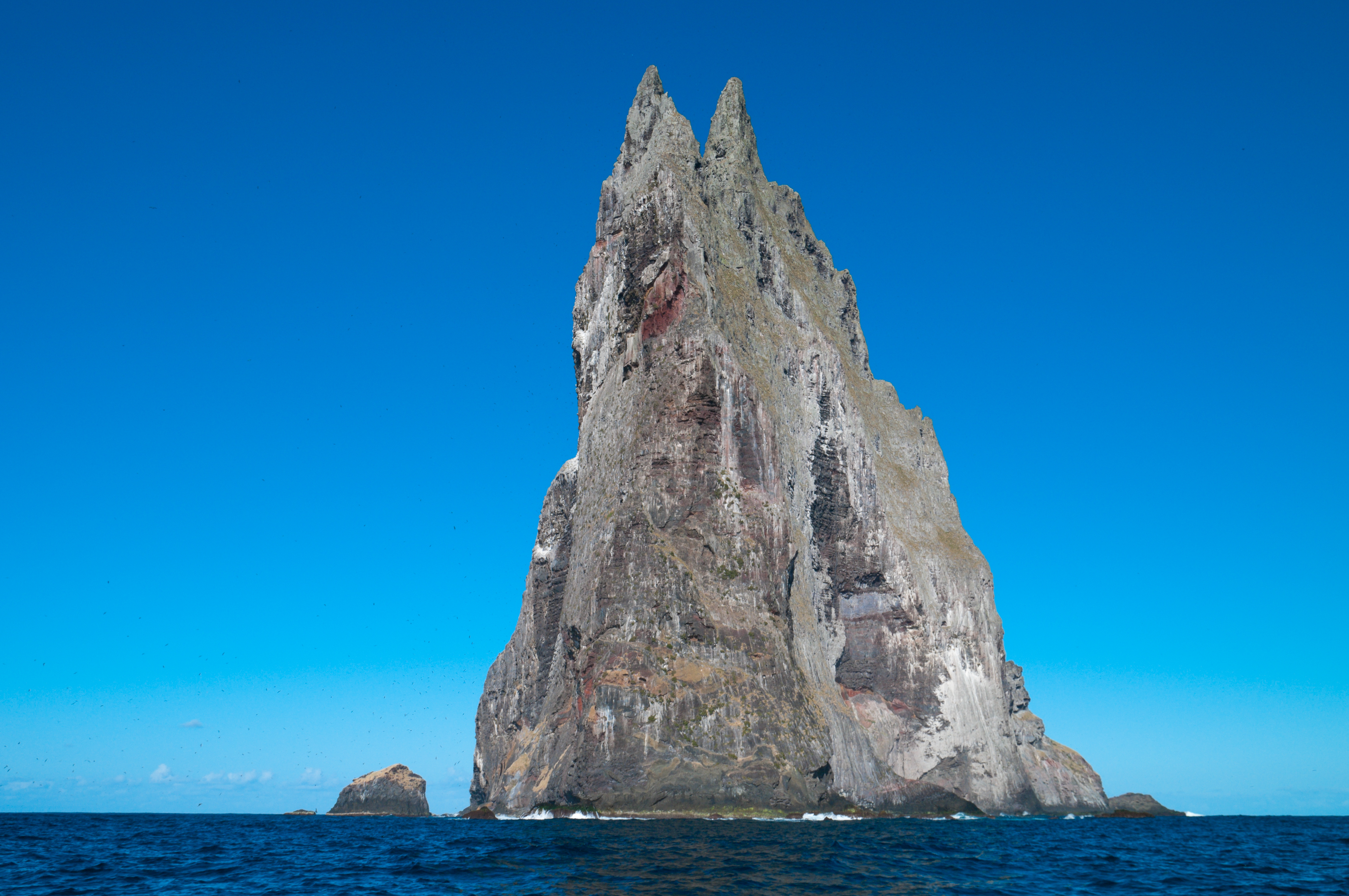 A very tall grey rock face pointing directly up out of the sea