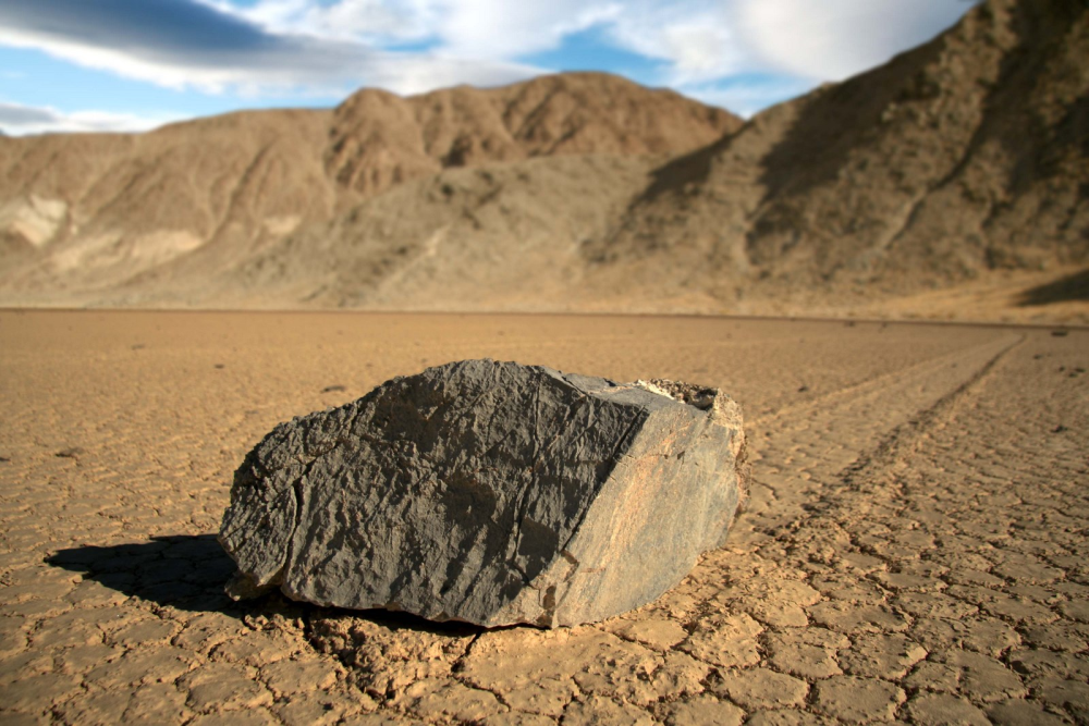 a sailing stone with a carved out mark behind it sitting on dry lakebed in racetrack playa