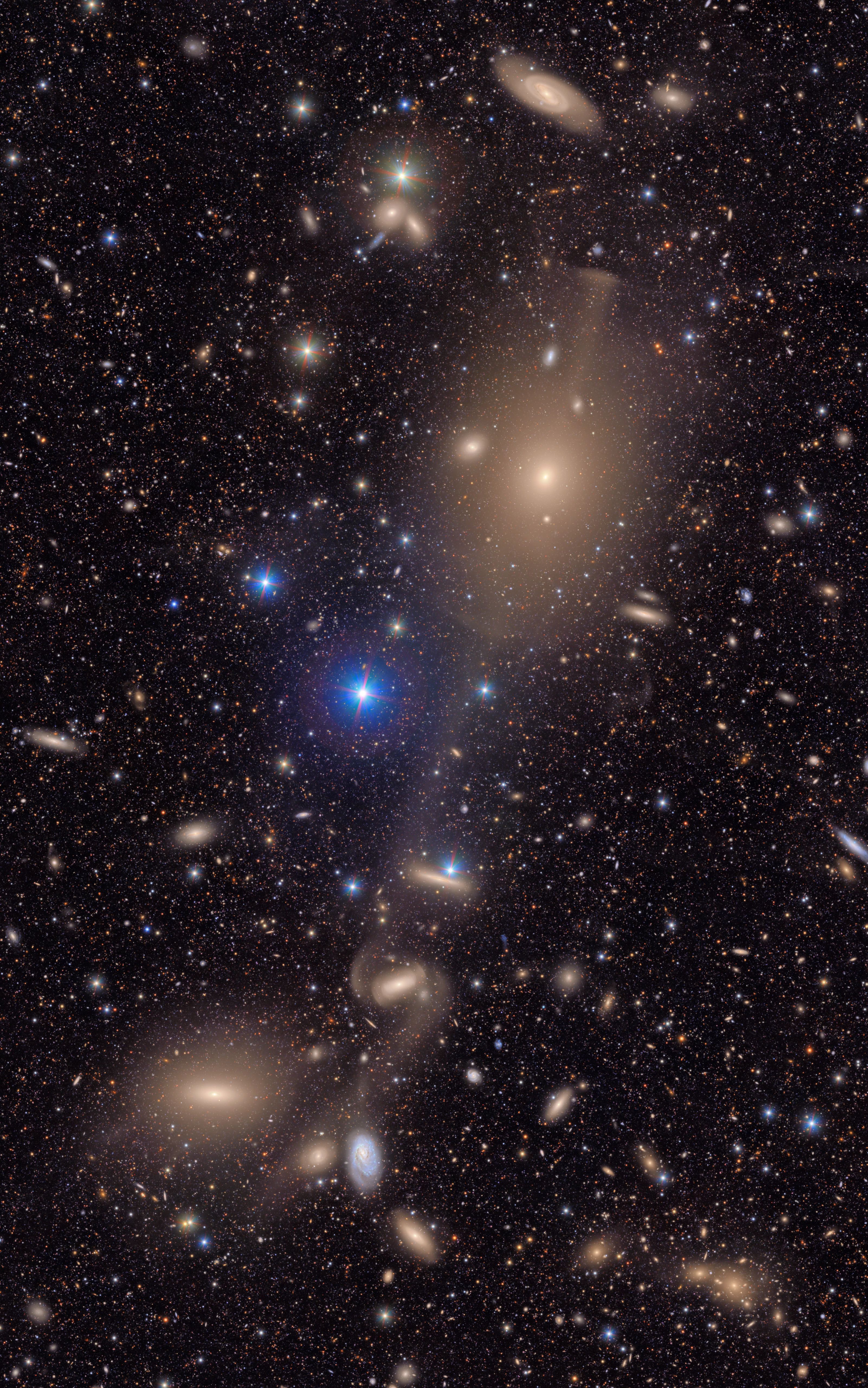 This image shows a small section of NSF-DOE Vera C. Rubin Observatory's total view of the Virgo cluster. Bright stars in the Milky Way galaxy shine in the foreground, and many distant galaxies are in the background. Four galaxies, one of the enormous, are connected by a bridge of gas