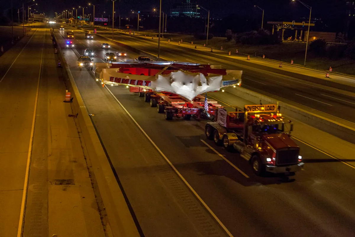 A truck carrying the acclerator ring which spans four lanes across a freeway at night. A truck carrying the acclerator ring which spans four lanes across a freeway at night.