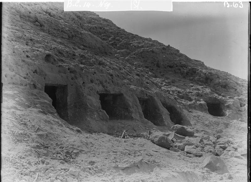 A black and white photo showing the tomb where the individual was found. The tomb consists of four square spaces carved into the rocky hillside face. There is a firth space slightly further along. 