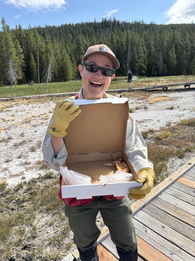 Yellowstone National Park Geology Program volunteer Tara Cross smiles and shows off a pizza box found on Geyser Hill in Upper Geyser Basin Yellowstone National Park Geology Program volunteer Tara Cross smiles and shows off a pizza box found on Geyser Hill in Upper Geyser Basin