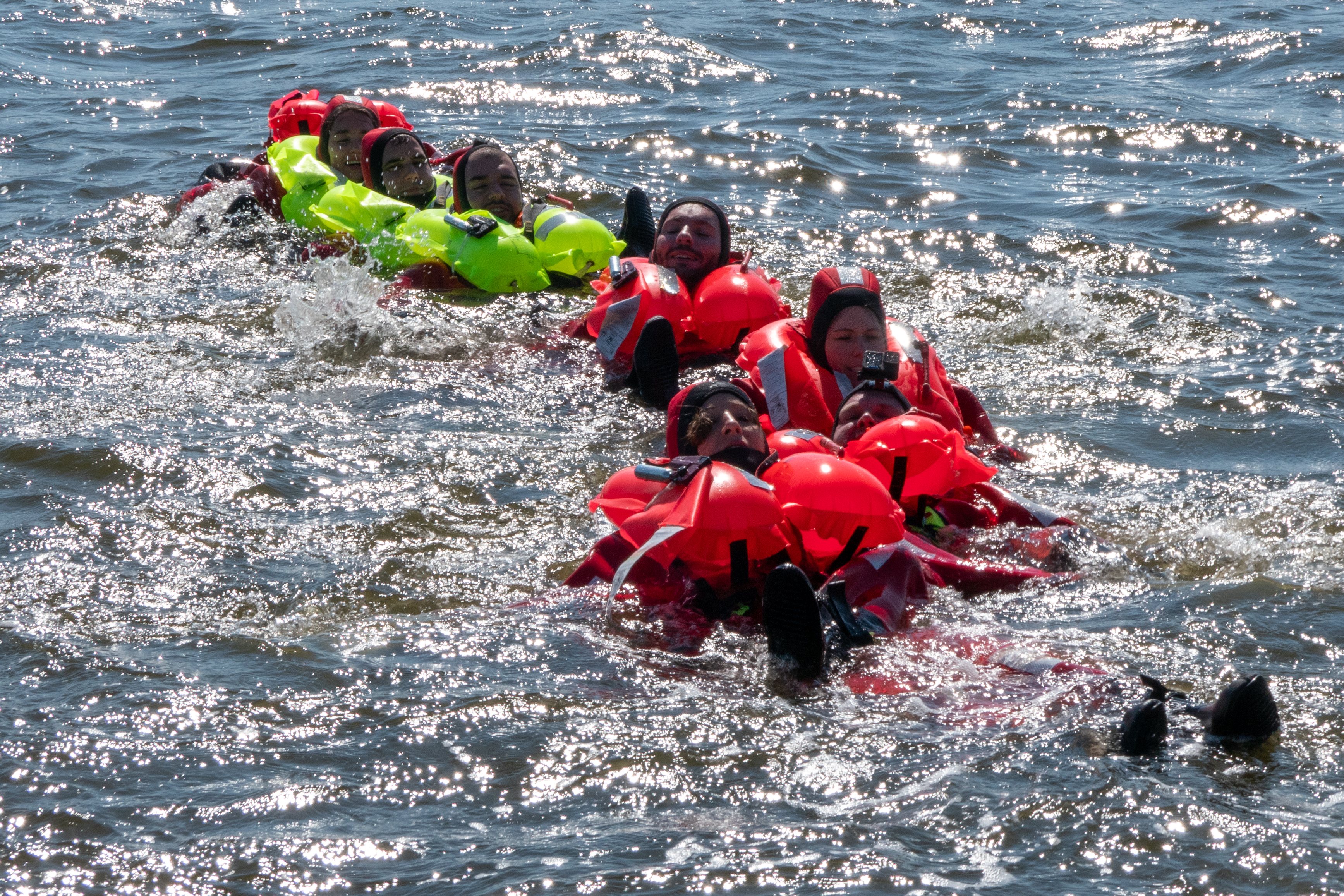 Seven people are in the ocean with inflatable life jackets all hanging to each other in a line Seven people are in the ocean with inflatable life jackets all hanging to each other in a line