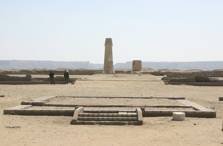 stone structures in the desert including a tall monument and the remains of some steps, with two people standing in the middle distance stone structures in the desert including a tall monument and the remains of some steps, with two people standing in the middle distance