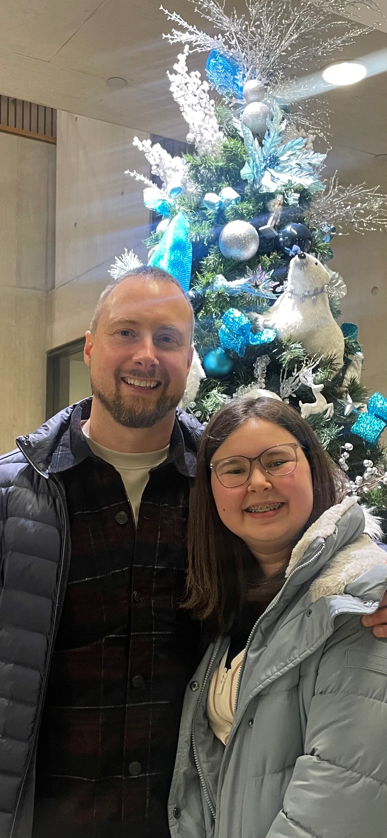 young girl and her father standing in front of a christmas tree decorated with blue and silver ornaments young girl and her father standing in front of a christmas tree decorated with blue and silver ornaments