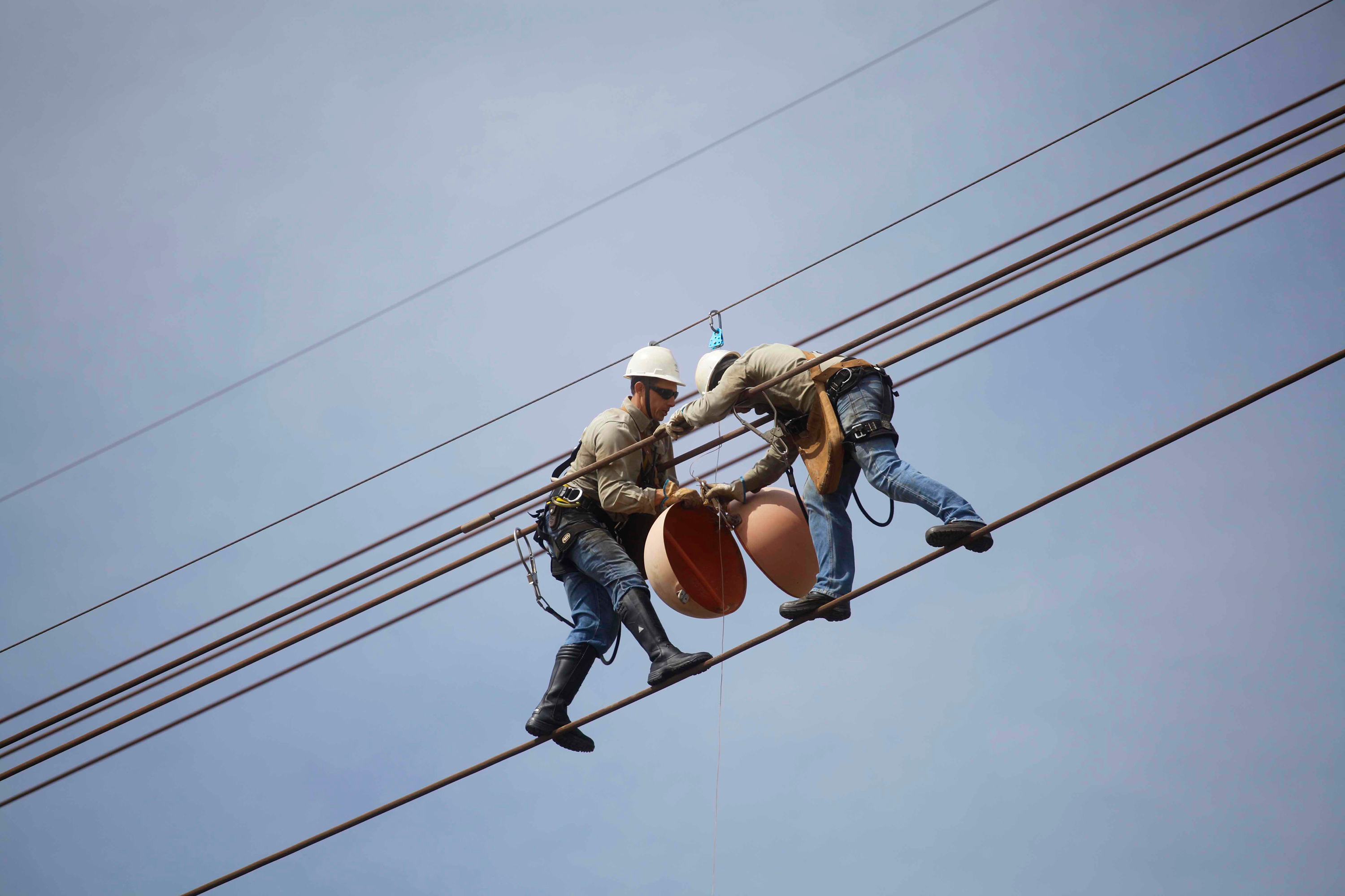 Two workers on a power line stalling a big marker ball